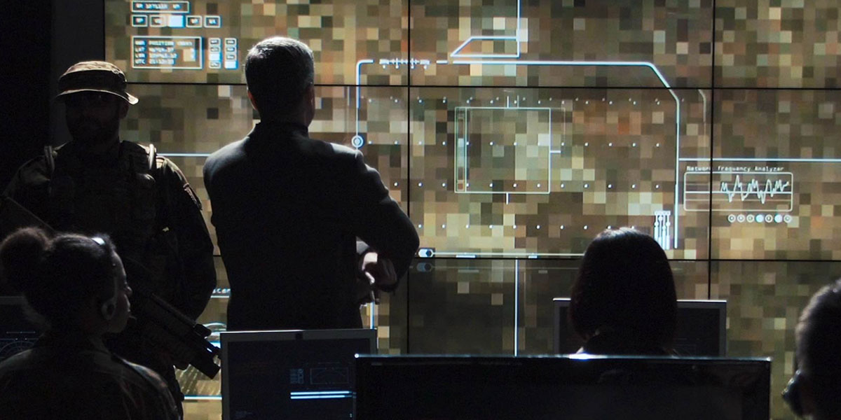 military service members standing and sitting at computers and reviewing a large screen on the wall