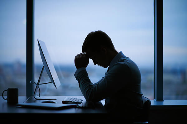 Silhouette of man resting forehead on hands