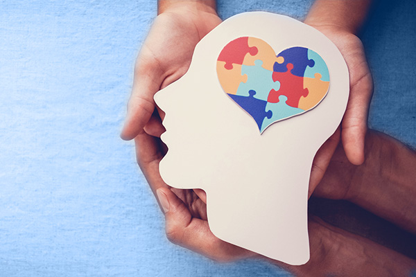 hands holding a white silhouette head shape with a heart-shaped puzzle