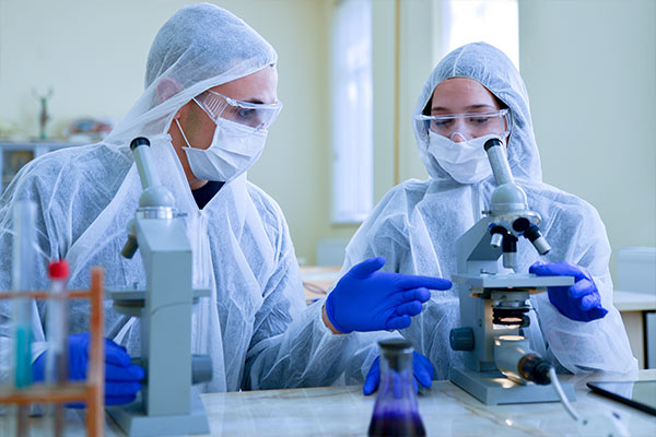 Two scientists in full PPE inspecting microscope