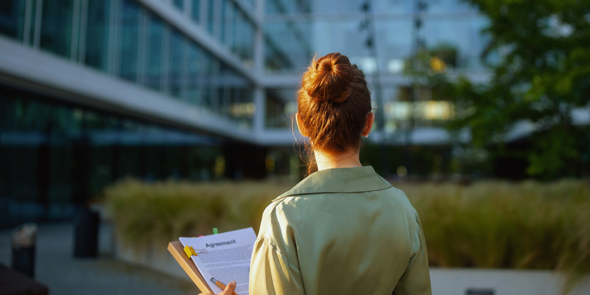 sustainability professional holding documents and standing in front of a courtyard and office building